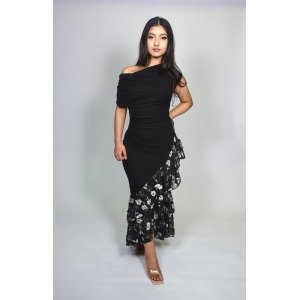 Woman wearing a black off-the-shoulder ruched midi dress with an asymmetrical black floral chiffon ruffle hem and clear heels.